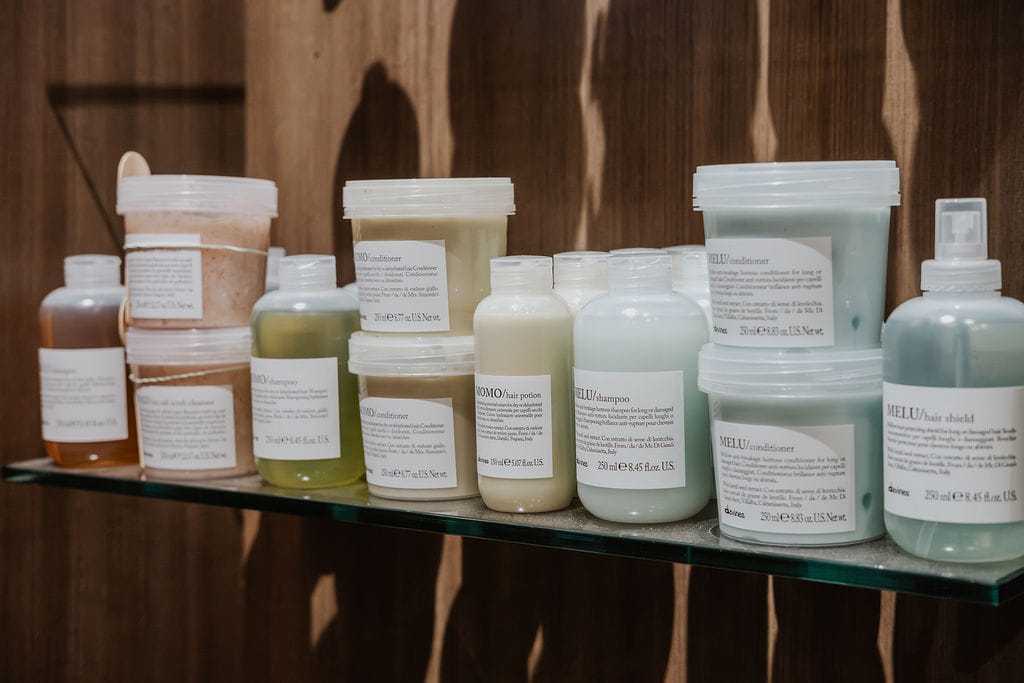 Several bottles and tubs of hair care products on a glass shelf.