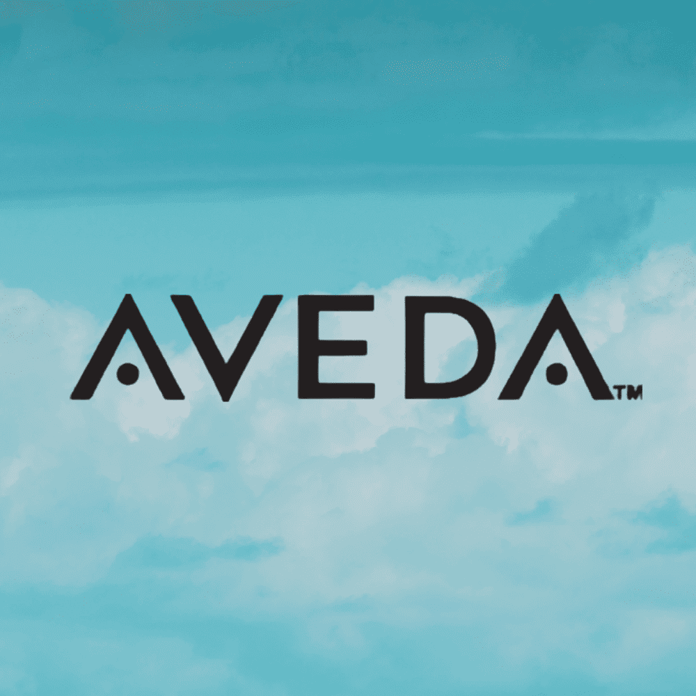 Aveda logo against a sky blue background with clouds.