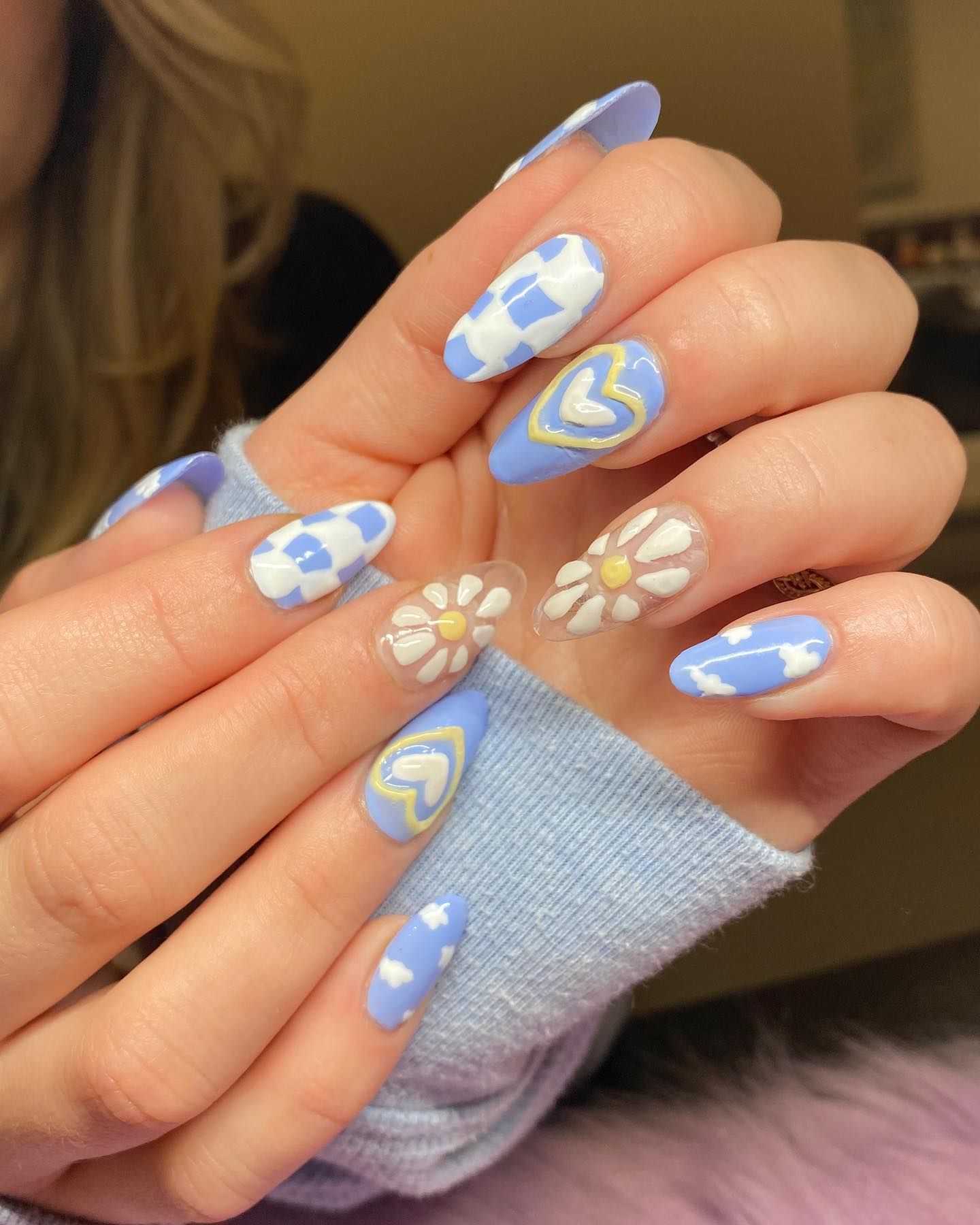 Hands with long blue and white nails featuring flowers, hearts, and checkered designs.