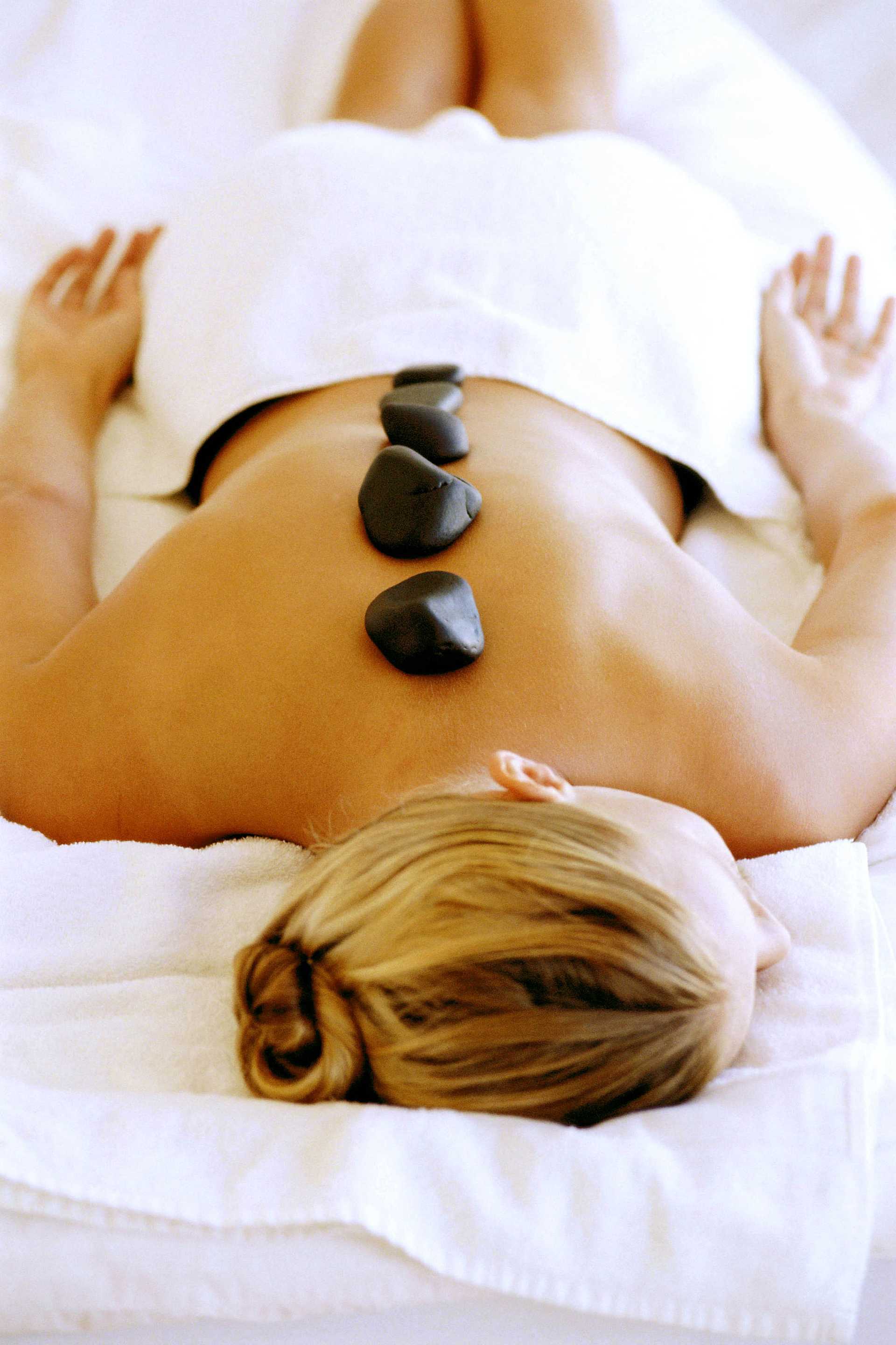 Woman receiving a hot stone massage on her back, lying on a white towel, in a spa setting.