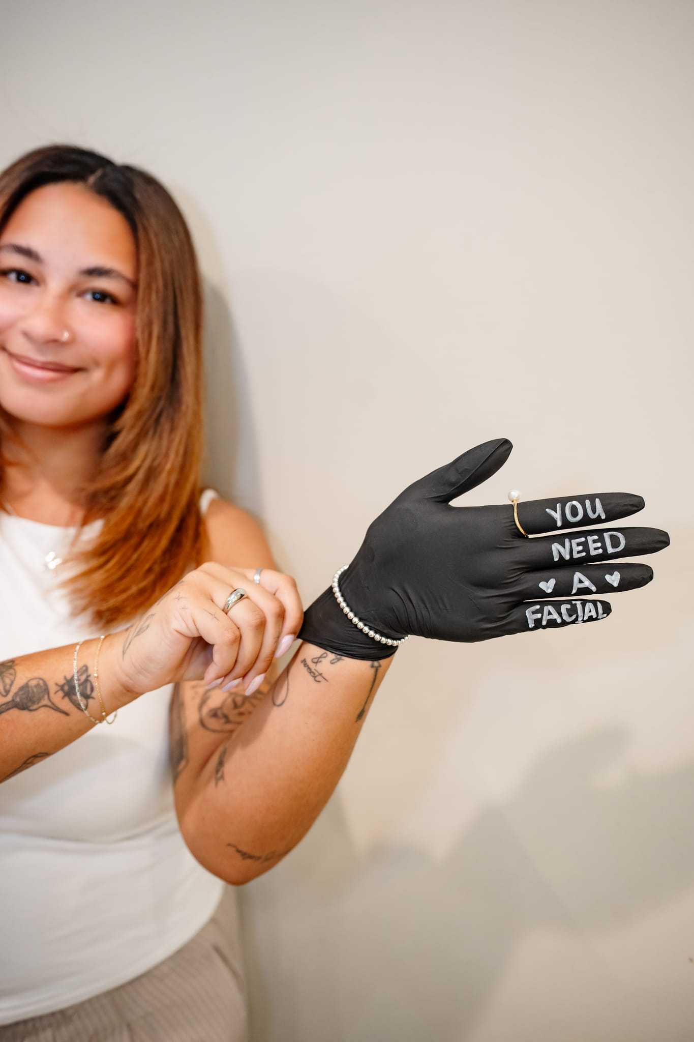 A person shows a glove with "You need a facial" written on it, smiling in a spa setting.