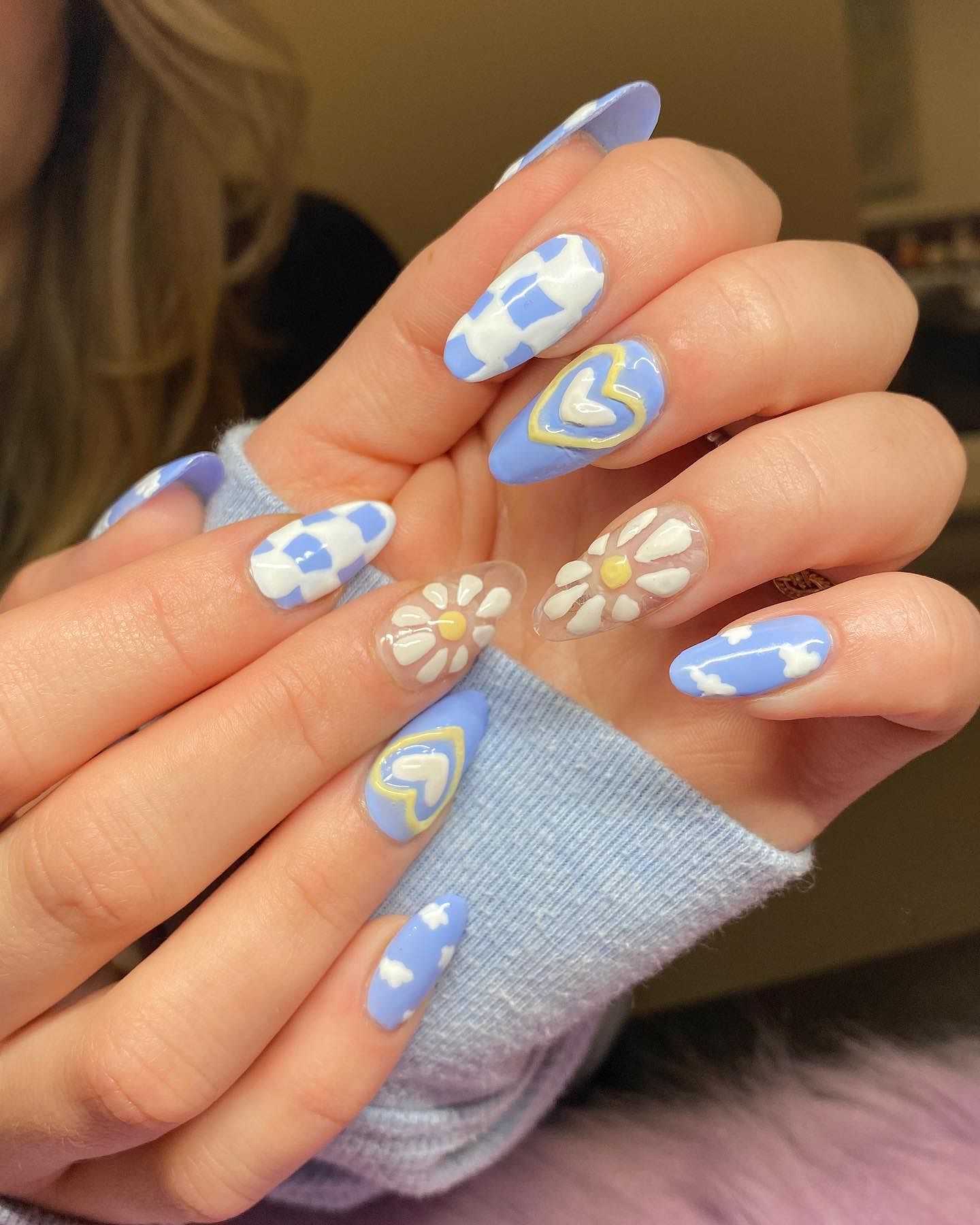 Hands with long blue and white nails featuring flowers, hearts, and checkered designs.