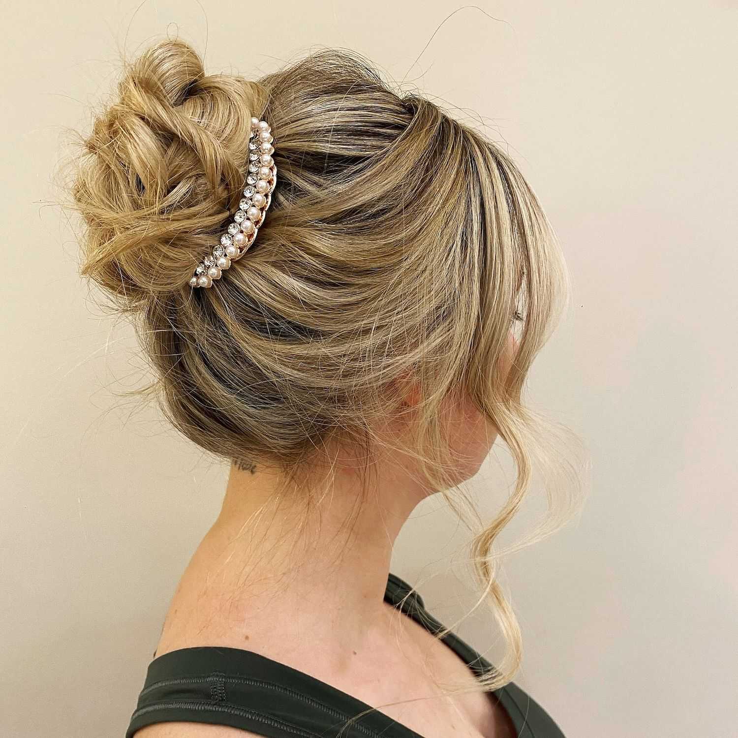 Woman with an intricate updo hairstyle adorned with a pearl hair accessory, viewed from the side.