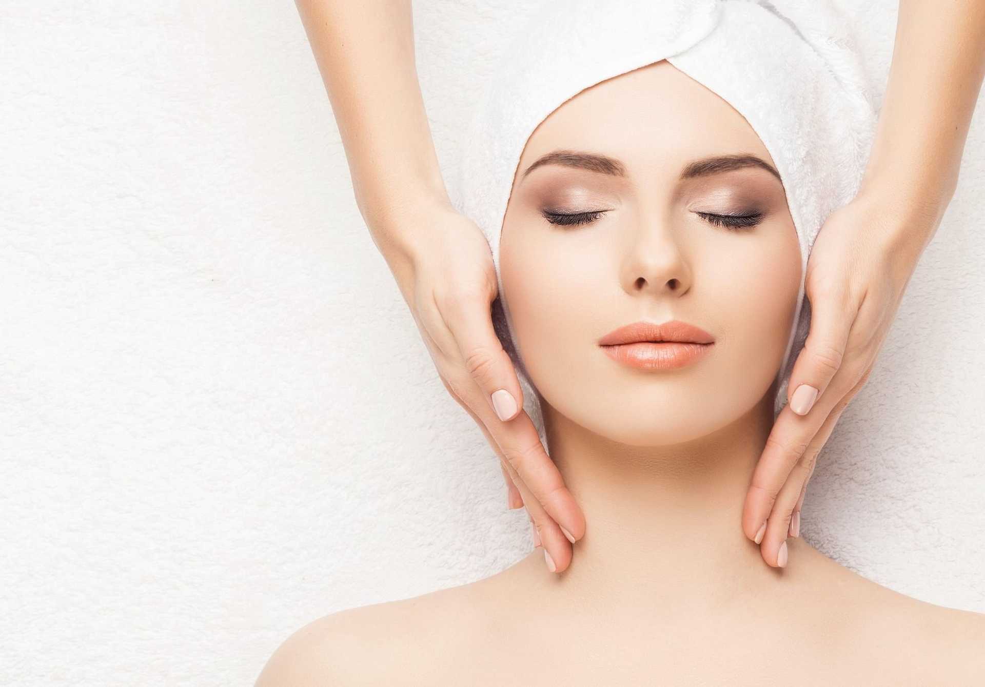 Woman with towel on head receiving facial massage in spa setting.